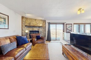 A living room with a leather sofa, a wooden coffee table, a fireplace, a television, and a balcony with a view. - Mountain Getaway condo with wood burning fireplace close to adventure (Granby)