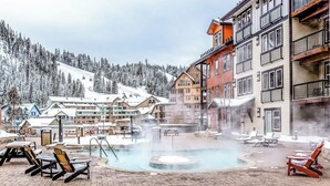 A hotel with a hot tub, outdoor seating, and a view of snowy mountains.