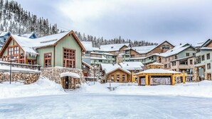 A snow-covered village with wooden buildings, a frozen lake, and a mountainous backdrop.