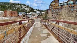 A bridge leading to a building complex with multiple floors and a mountainous backdrop.