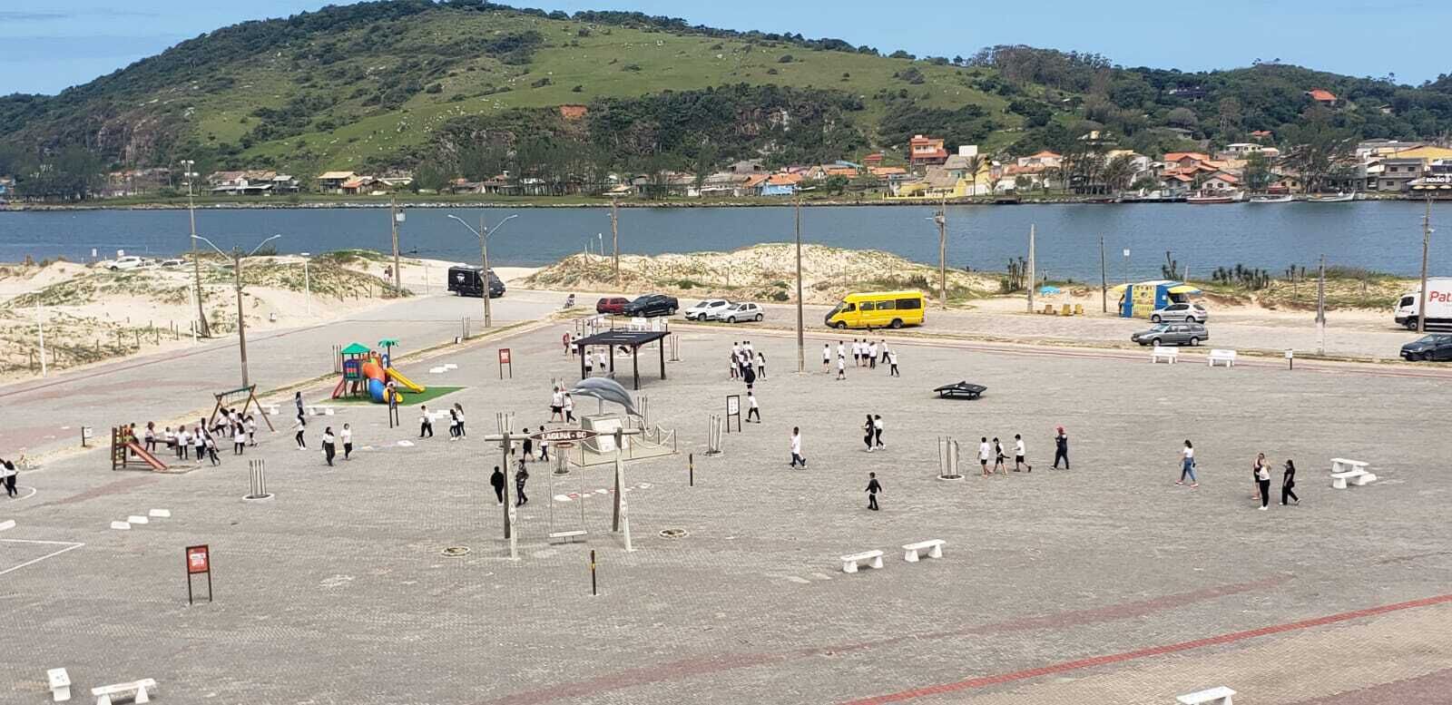 Ein Parkplatz mit Spielplatz, Bushaltestelle und Blick auf See und Hügel.