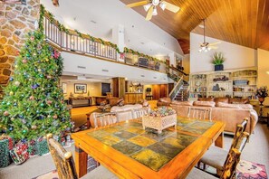 Ein geräumiger Wohnbereich mit einem großen Esstisch aus Holz, einem Weihnachtsbaum und einer Treppe, die zu einer oberen Ebene führt.
