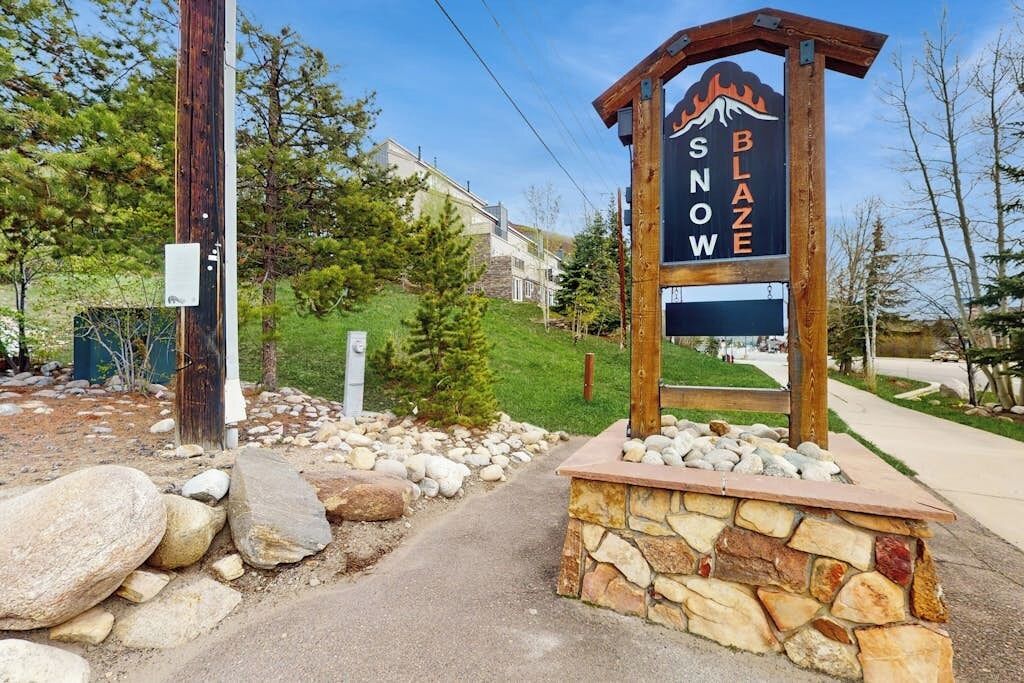 A wooden sign with 'SNOW' and 'BLAZE' text, a stone base, and a paved path leading to a building.
