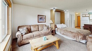 Een kamer met een bank, een bed, een houten salontafel, een lamp en een ingelijst beeld aan de muur.