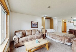 A room with a sofa, a bed, a wooden coffee table, a lamp, and a framed picture on the wall. - Studio on the Shuttle Route with WiFi and Shared Pool, Hot Tubs, and Gym (Winter Park)