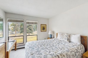 Een slaapkamer met een bed, bureau, lamp en raam met jaloezieën.