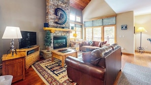 A living room with a stone fireplace, leather sofa, wooden coffee table, and a television. - End-Unit Townhome on Shuttle Route w/WiFi/Shared Pool/Hot Tub - 1 Mile to Slopes (Keystone)