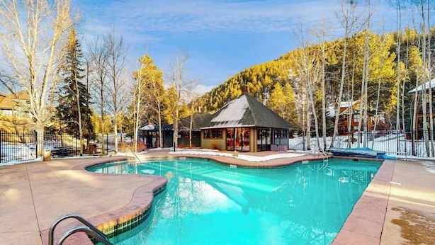 A swimming pool with a metal ladder, surrounded by a fence, and a building with a gazebo-like structure in the background. - End-Unit Townhome on Shuttle Route w/WiFi/Shared Pool/Hot Tub - 1 Mile to Slopes (Keystone)