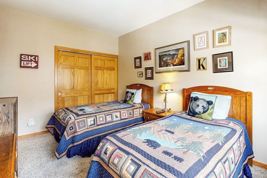 A bedroom with two beds, a wooden wardrobe, a ski lift sign, and framed pictures on the wall.