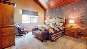 A bedroom with a sloped ceiling, a brick wall, a bed with a quilt, a rocking chair, a nightstand, and a window with a blind. - End-Unit Townhome on Shuttle Route w/WiFi/Shared Pool/Hot Tub - 1 Mile to Slopes (Keystone)