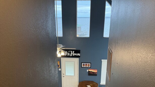Una escalera conduce a una habitación con un cartel que dice 'Lake House', una puerta, una pequeña mesa y vistas del cielo a través de ventanas.
