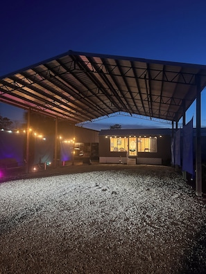 A covered outdoor area with a gravel floor, a building with a glass facade, and string lights.