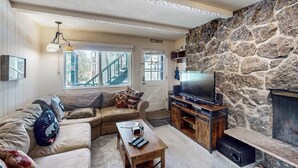 Ein Wohnzimmer mit Steinwand, einer Couch, einem Couchtisch, einem Fernseher und einem Kamin.