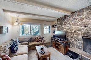 A living room with a stone wall, a sofa, a coffee table, a TV, and a fireplace.
