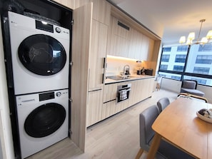 A modern kitchen with built-in appliances, a dining area with a table and chairs, and a view of the city through large windows. - D2102 - Modern Skyline Corner Suite with Pool & Gym in Downtown Miami (Miami)