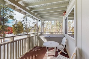 Ein überdachter Balkon mit Tisch und zwei Stühlen, einem roten Teppich und Blick auf Bäume und ein Gebäude.