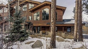 Une maison en rondins moderne, à plusieurs niveaux, dotée de grandes fenêtres et d’une fondation en pierre.