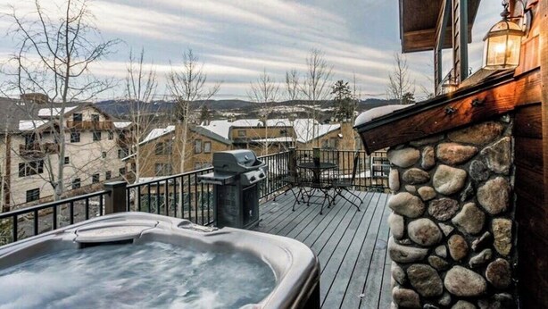 Un bain à remous sur une terrasse en bois, avec des murs en pierre, donnant sur un quartier résidentiel.