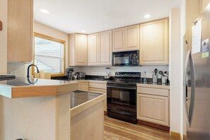 Eine moderne Küche mit Holzausstattung, einem Edelstahl-Kühlschrank, einer Mikrowelle, einem Backofen und einer Glasinsel-Arbeitsfläche.