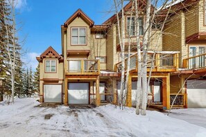 Ein mehrstöckiges Holzhaus mit Garage, Balkon und einer verschneiten Auffahrt.