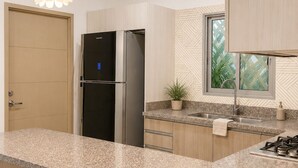 Une cuisine moderne dotée de plans de travail en granit, d’un réfrigérateur encastré, d’une cuisinière à gaz et de luminaires suspendus.