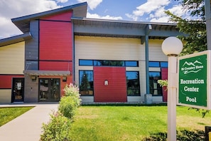Ein modernes Gebäude mit roter und beiger Fassade, einem Schild für 'Hi Country Haus Recreation Center Pool' und einem gepflegten Rasen.