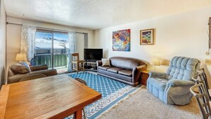 A living room with a sofa, armchair, TV, and a dining table. - Mountain view condo w/ a shared pool, hot tub, Ping-Pong, & pool table (Dillon)