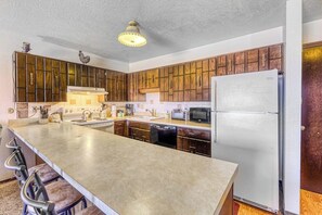 Eine Küche mit Holzausstattung, einem Edelstahlkühlschrank, einer Mikrowelle und einer Bar mit Barhocker.