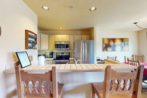 A modern kitchen with stainless steel appliances, a dining area with wooden chairs, and a wall-mounted artwork. - Wildernest Condo Close to Top Ski Resorts  + Free WiFi (Silverthorne)