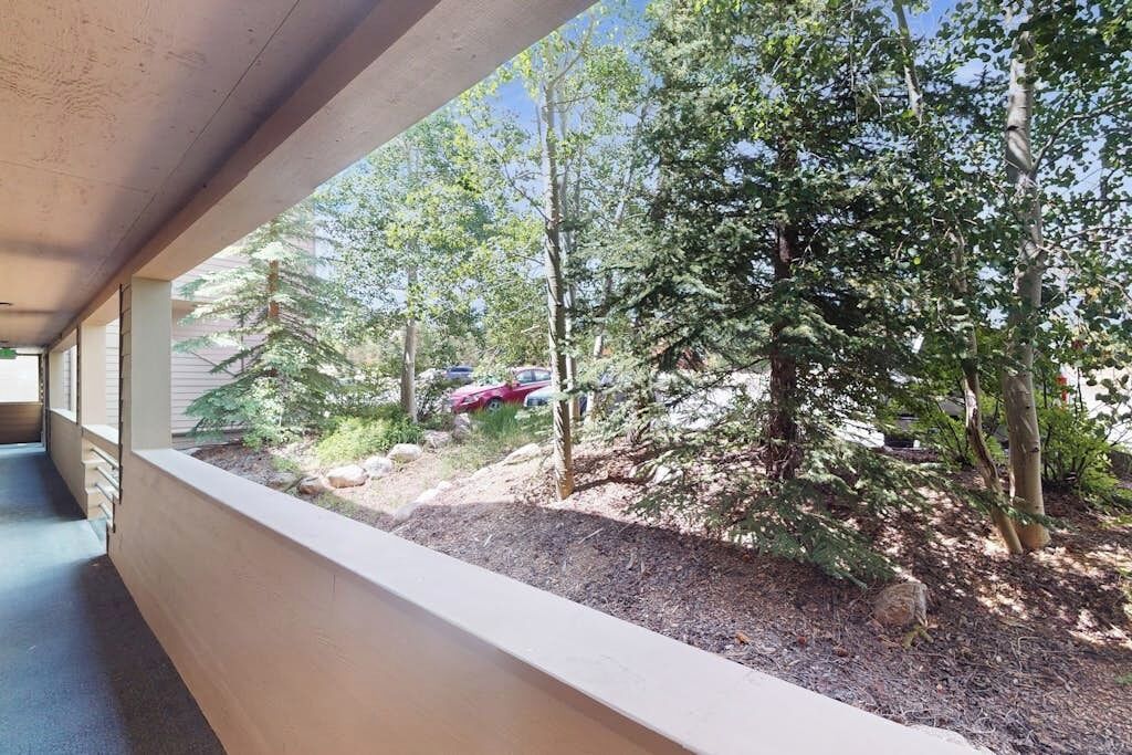 A covered outdoor area with a view of a wooded area and parked cars.