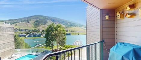 A balcony with a view of a lake and mountains, a covered outdoor seating area, and a pool.
