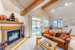 A living room with a fireplace, a sofa, a coffee table, and a dining area with chairs. - Blue River condo with water-view balcony, walking distance to the outlets (Silverthorne)