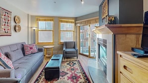 A living room with a sofa, armchair, small round table, and a patterned rug. - Walk to Slopes from Cozy Condo with Pool, Hot Tub, & Fitness (Keystone)