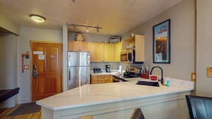A compact kitchen with a central island, built-in appliances, and a wooden door. - Walk to Slopes from Cozy Condo with Pool, Hot Tub, & Fitness (Keystone)