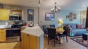 A modern kitchen with a built-in microwave, oven, and sink. There is a dining area with a table and chairs, and a living room with a sofa and a chandelier. - Walk to Slopes from Cozy Condo with Pool, Hot Tub, & Fitness (Keystone)