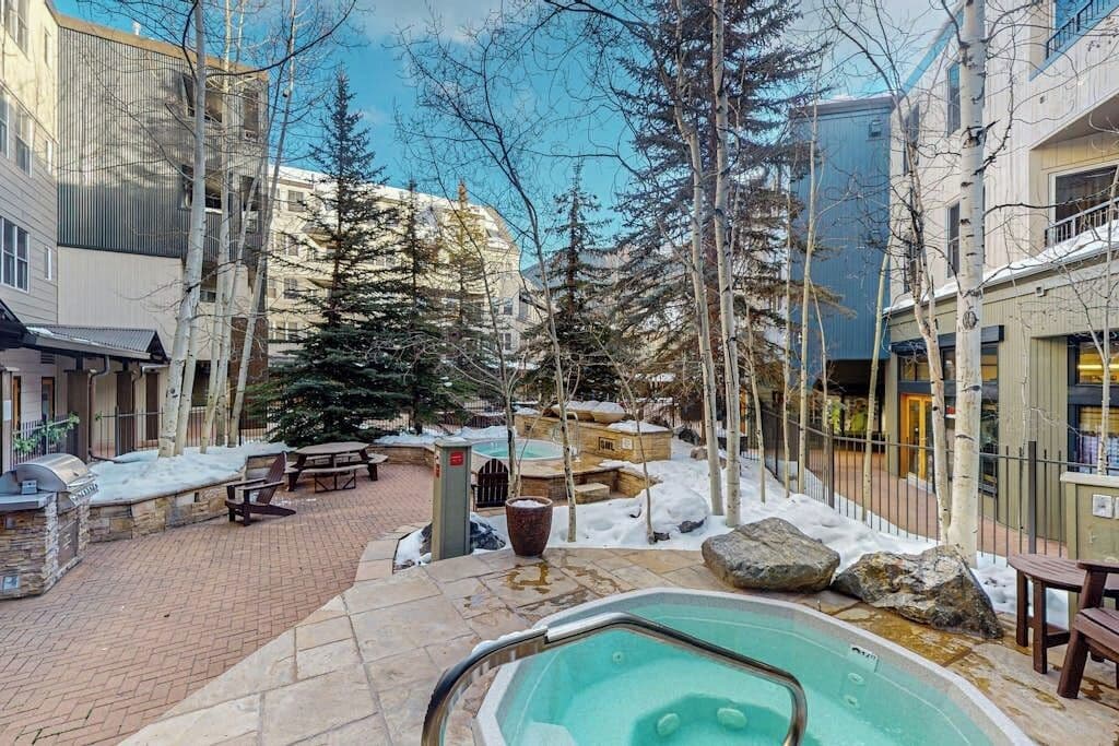 A pool area with a hot tub, stone benches, and snow-covered ground.