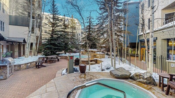 A pool area with a hot tub, stone benches, and snow-covered ground. - Walk to Slopes from Cozy Condo with Pool, Hot Tub, & Fitness (Keystone)