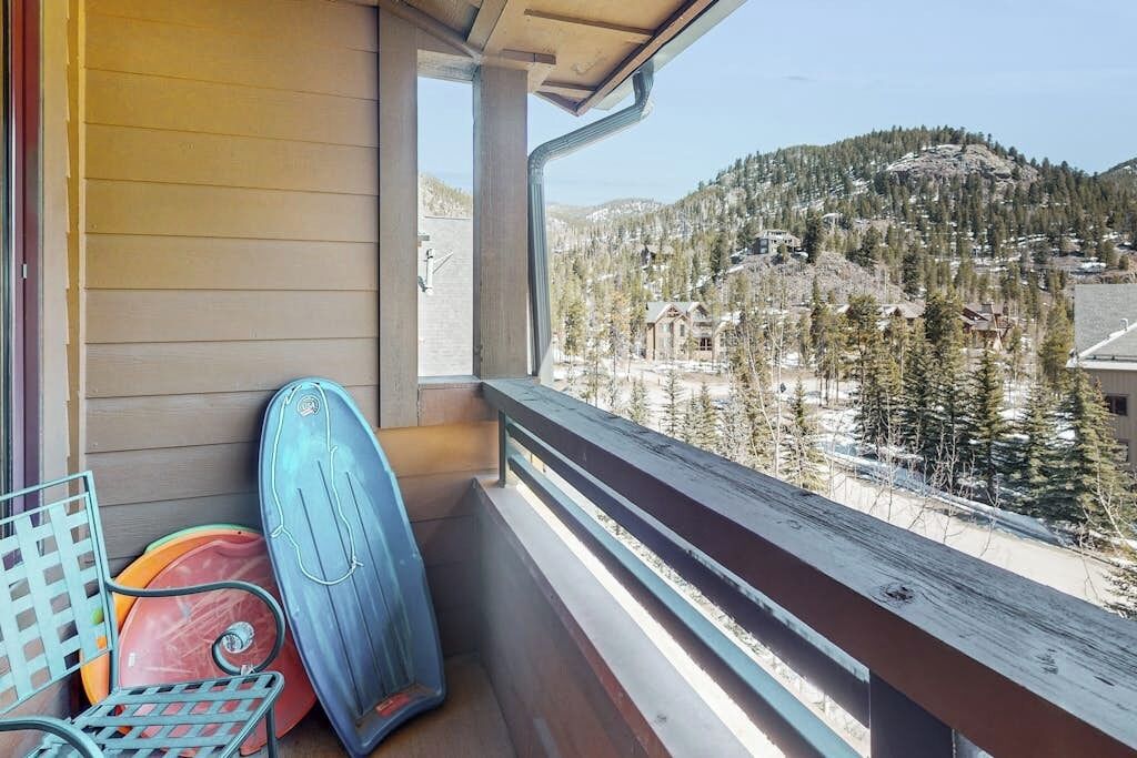 A balcony with a view of a mountainous landscape, a surfboard, and a chair.