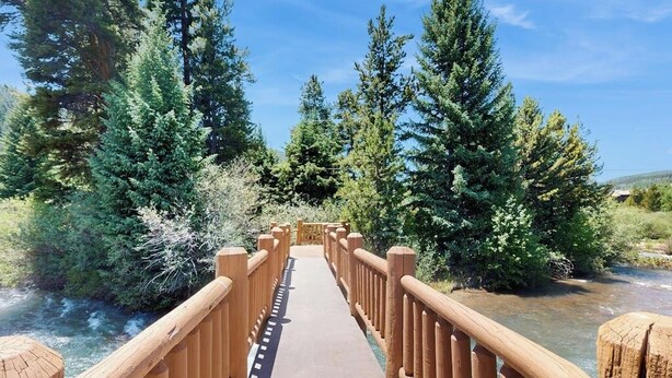 Un ponte di legno con ringhiere, immerso in una vegetazione lussureggiante e sotto un cielo sereno.