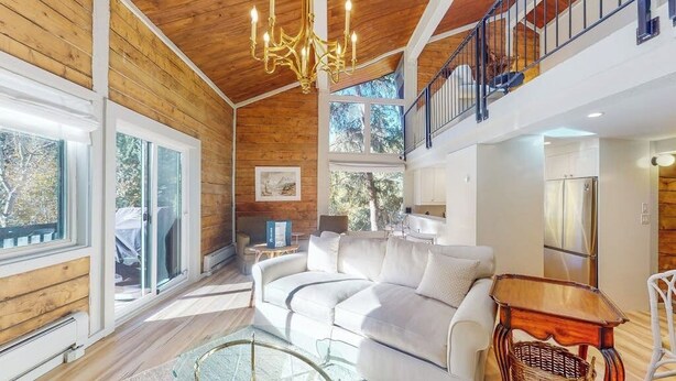 A spacious living area with a white sofa, a glass coffee table, and a wooden side table. - 2nd-floor chalet with fireplace, grill, balcony, washer/dryer, ski & mtn views (Vail)