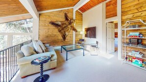 A spacious living area with a wooden ceiling, a mounted animal head, a sofa, a glass coffee table, and a bookshelf. - 2nd-floor chalet with fireplace, grill, balcony, washer/dryer, ski & mtn views (Vail)