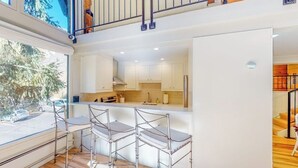 A modern kitchen with white cabinets, a bar area with metal stools, and a view of the outdoors. - 2nd-floor chalet with fireplace, grill, balcony, washer/dryer, ski & mtn views (Vail)
