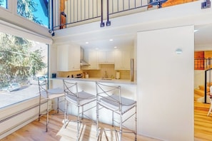 Eine moderne Küche mit weißen Schränken, einer Bar mit Metallhockern und Blick ins Freie.
