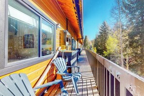 Eine Holzterrasse mit Adirondack-Stühlen, einem Hollerdeck und Blick auf Bäume.