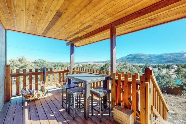 Eine Holzterrasse mit Tisch und Stühlen, mit Blick auf eine gebirgige Landschaft.
