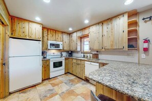 A kitchen with wooden cabinets, a refrigerator, a microwave, an oven, and a granite countertop.