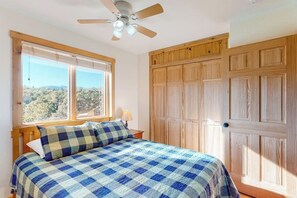 A bedroom with a bed, a ceiling fan, a window with a view, and wooden wardrobes.