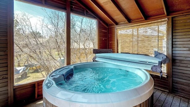 Un jacuzzi en una habitación de madera con ventanas amplias y vistas a árboles.