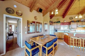 Ein Essbereich mit Holztisch und blauen Stühlen, eine Küche mit Holzausbau und eine Decke mit freiliegenden Balken.