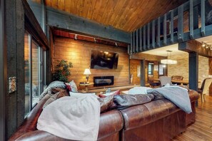 Ein gemütliches Wohnzimmer mit einer Ledersofa, einem an der Wand montierten Flachbildfernseher und einem Essbereich mit Stühlen und Tisch.